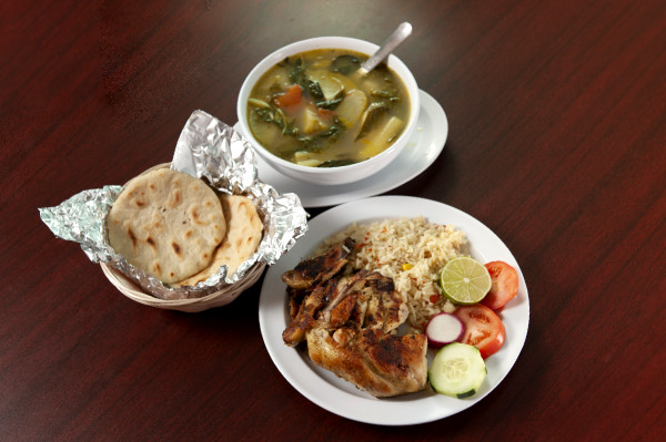 An overflowing plate of food, a bowl of soup, and a basket of pupusas.